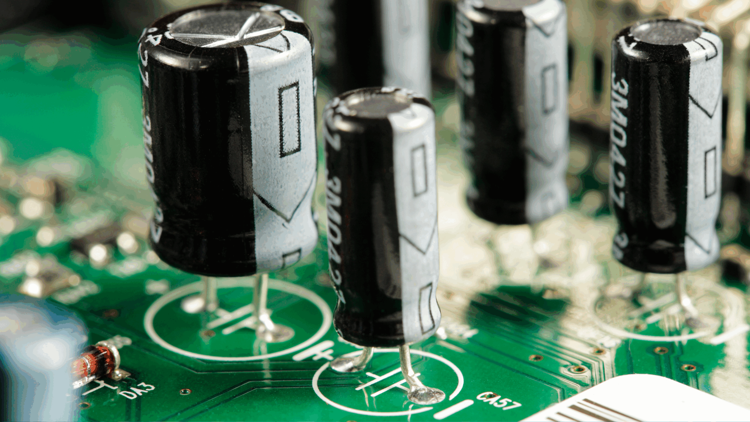 Un gros plan sur le circuit imprimé d'un appareil électronique, montrant plusieurs condensateurs et d'autres composants soudés.