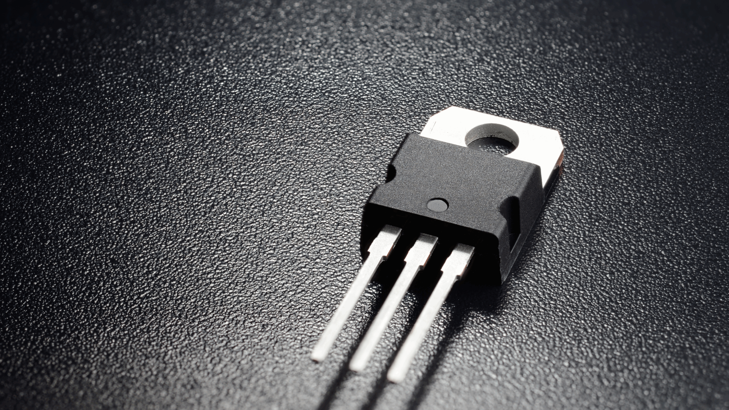 Gros plan sur un transistor bipolaire noir à trois broches (boîtier TO-92) avec des marquages, posé sur une surface réfléchissante.