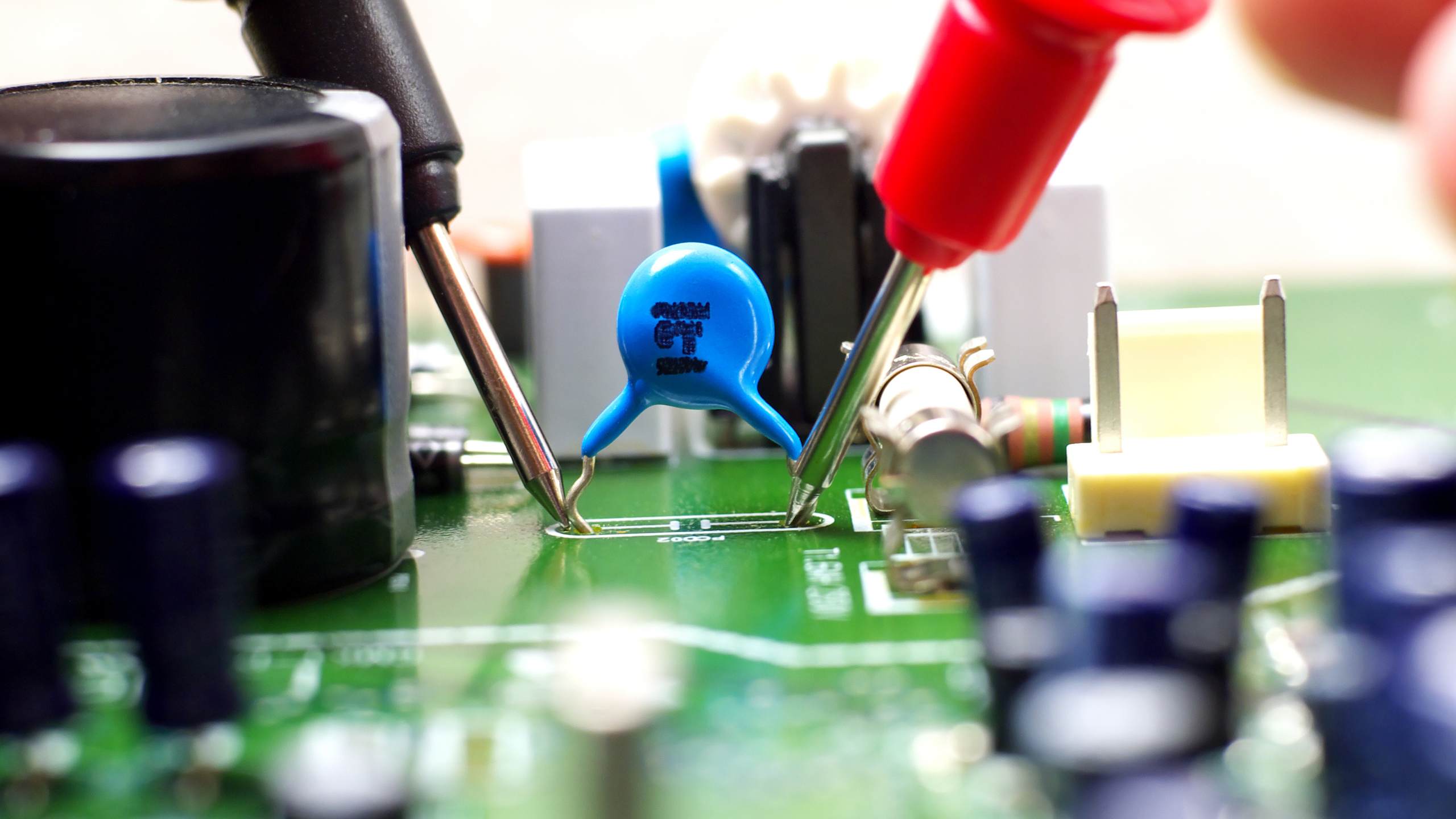 Test d'un condensateur HS céramique bleu avec des sondes de multimètre sur un circuit imprimé