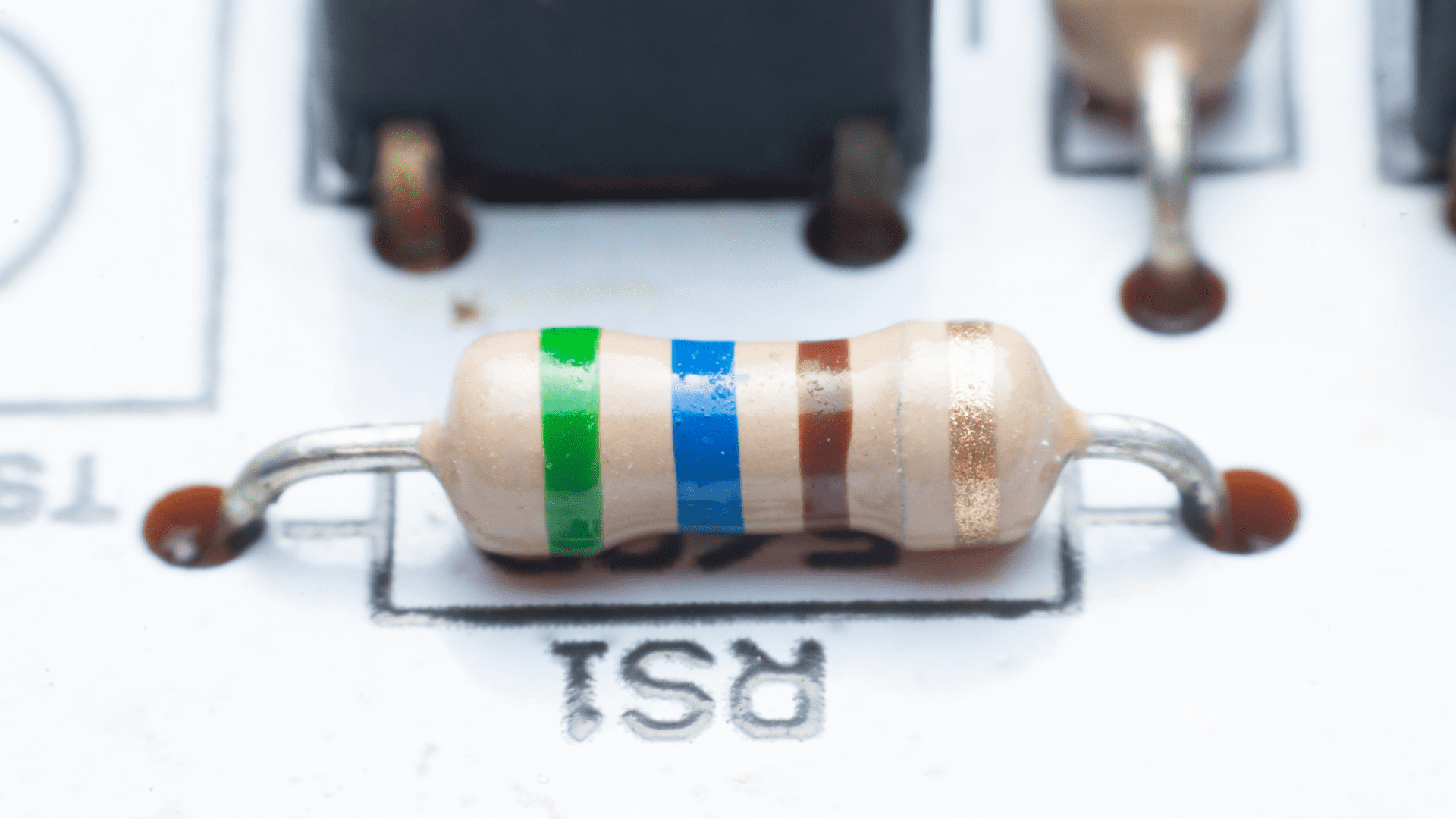 Gros plan d'un composant de résistance électrique classique avec ses anneaux de couleur, soudé sur un circuit imprimé.